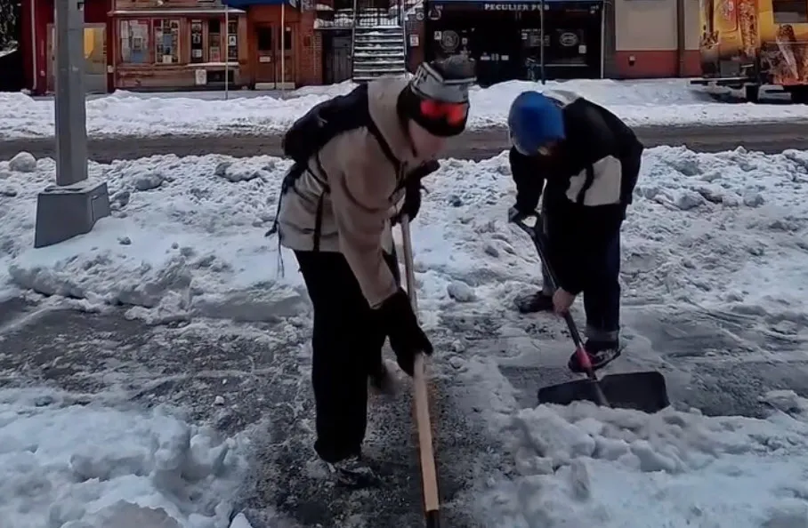 Two people clearing snow from a sidewalk.